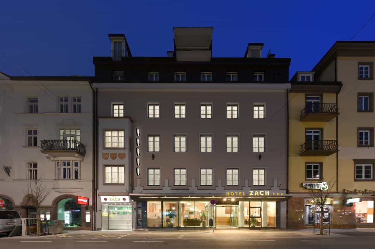 Hotel Zach illuminated at dusk on a city street with surrounding buildings