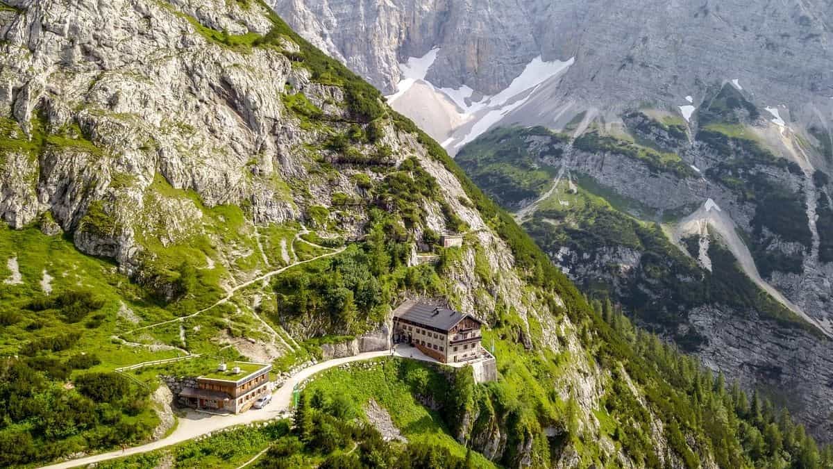 Karwendelhaus mountain hut nestled on a steep, green slope beneath rocky peaks with snow patches.