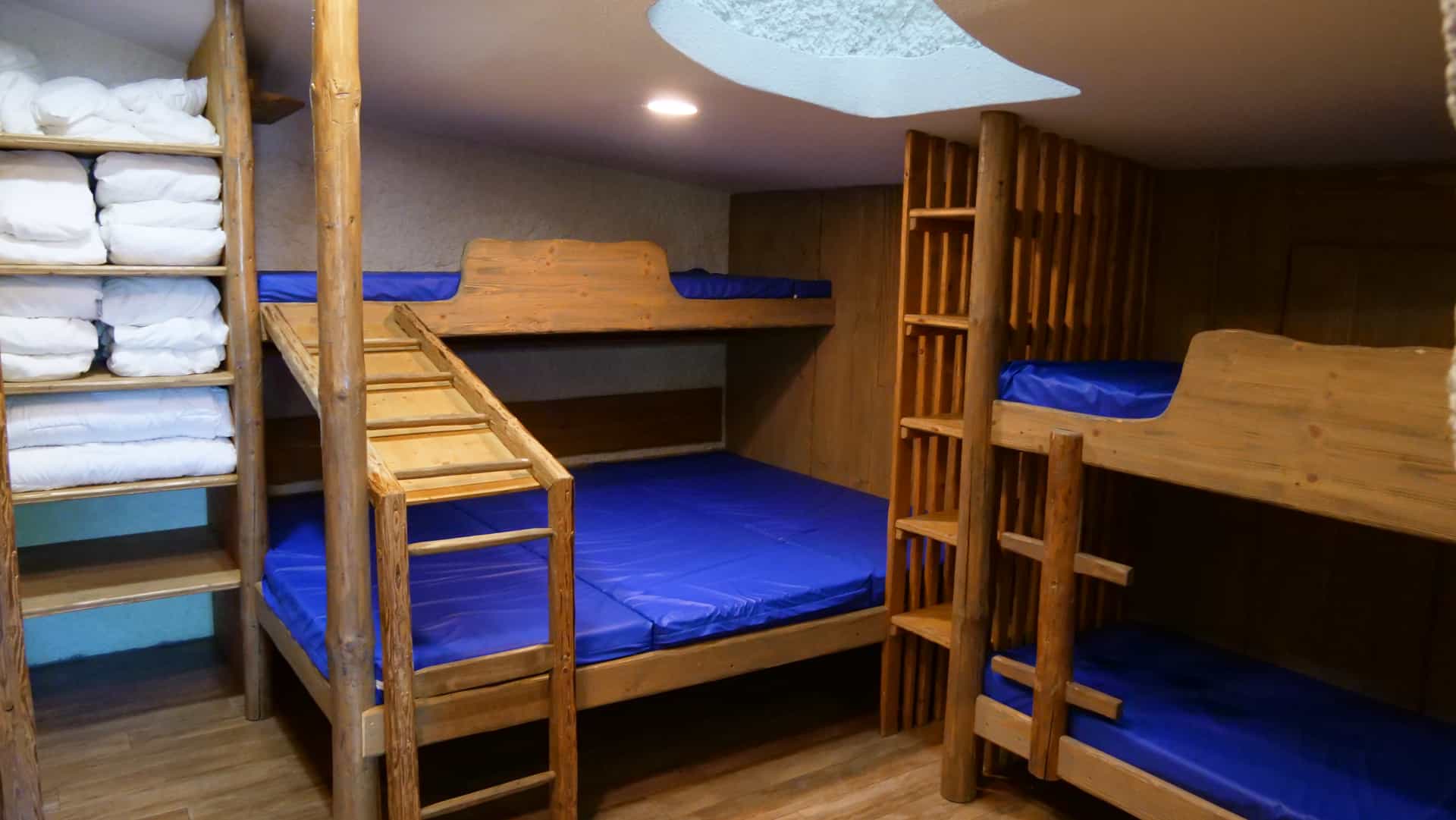 Wooden bunk beds with blue mattresses and stacked white linens in a rustic cabin room