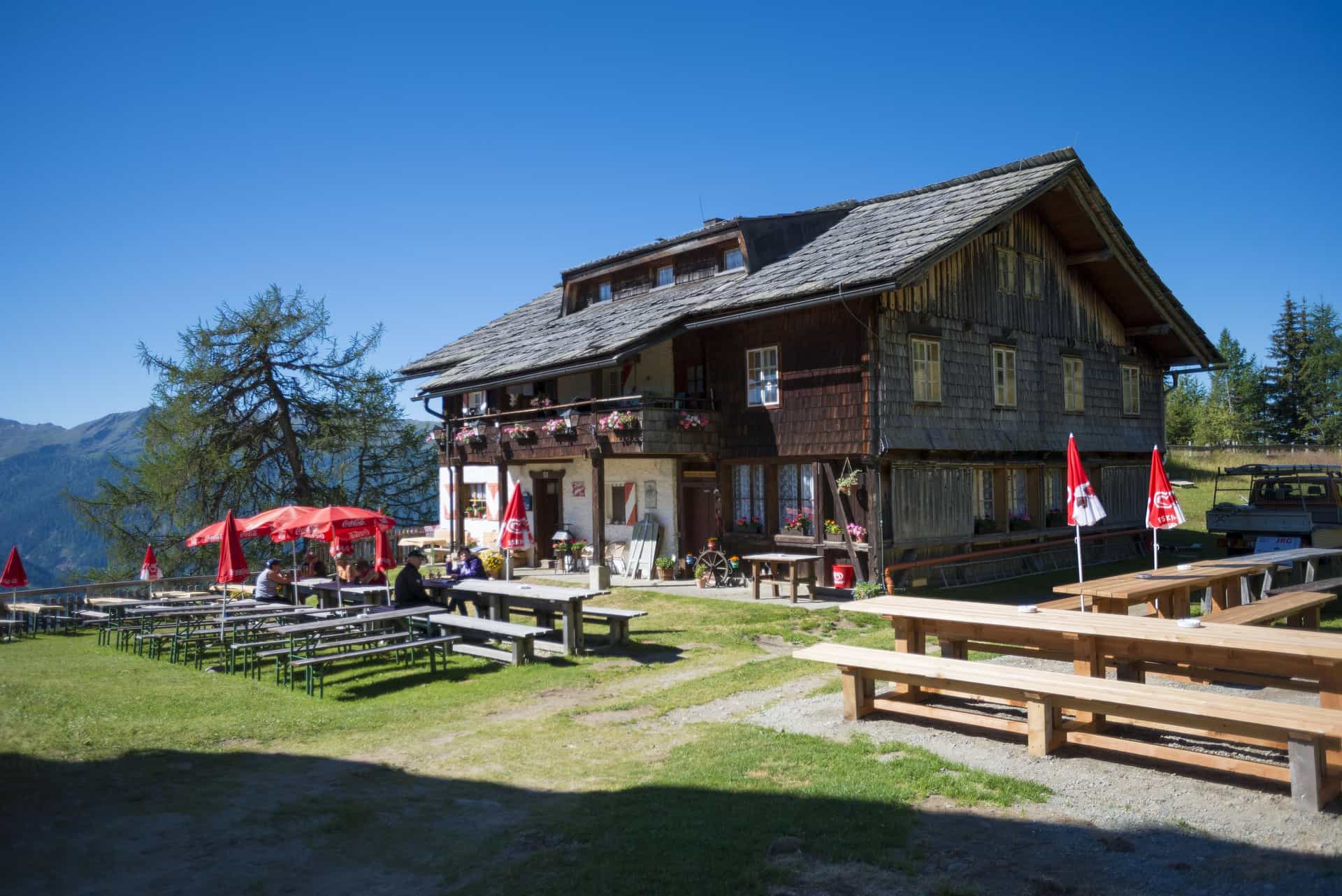 Alpengasthaus Marterle with outdoor seating and mountain backdrop under a clear blue sky.