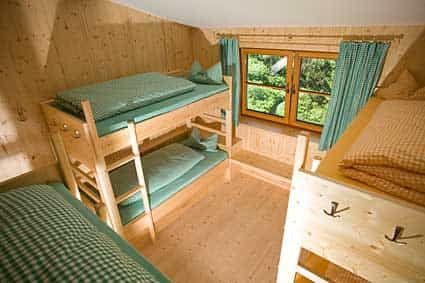 Wooden bunk beds with green checkered bedding inside an attic room with a view of green trees.