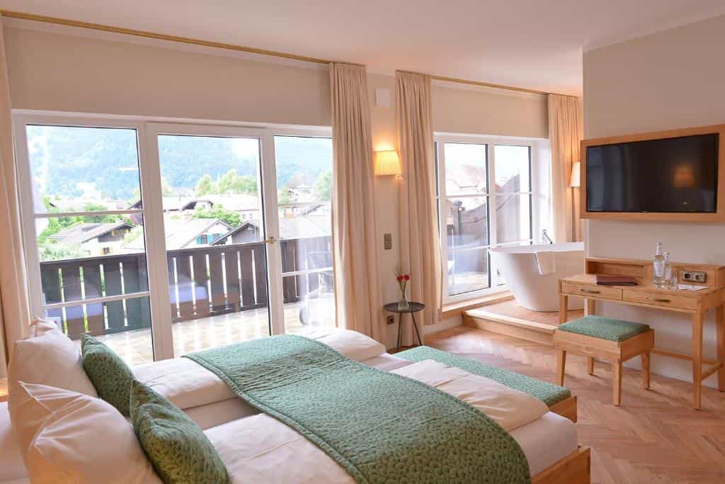 Hotel room with bed, desk, TV, and freestanding bathtub with mountain view.