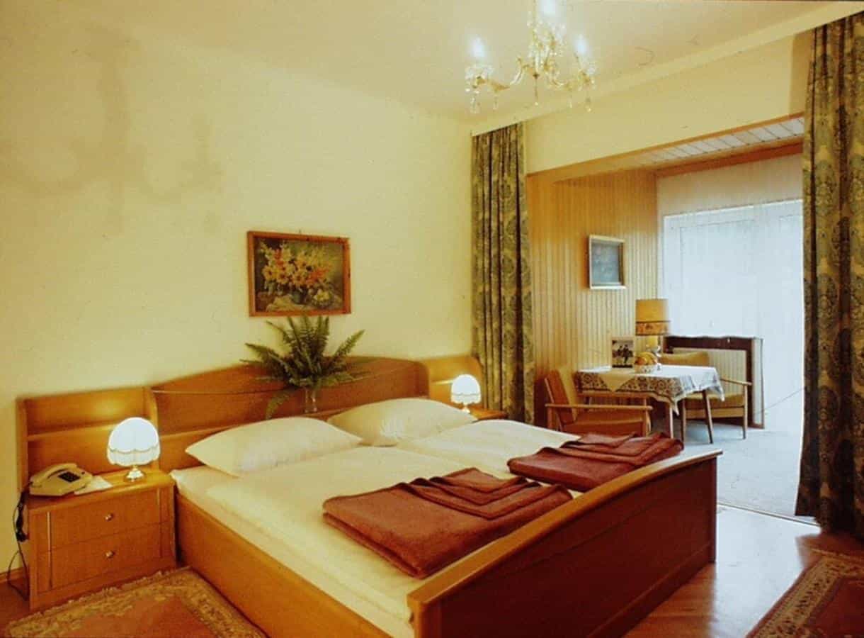 Twin beds with white linens in a hotel room with wood furniture and chandelier.