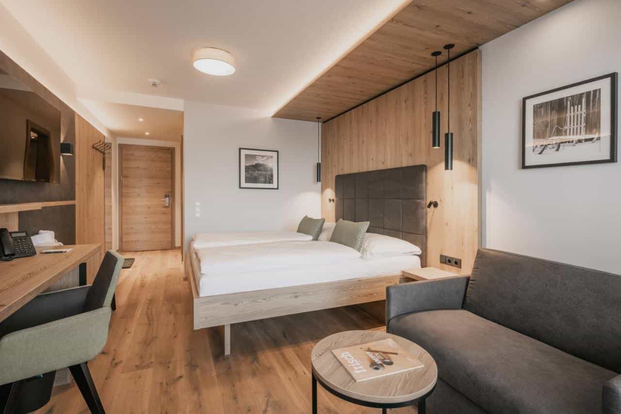 Modern hotel room with twin beds, wood paneling, and a grey sofa, Zauchensee.