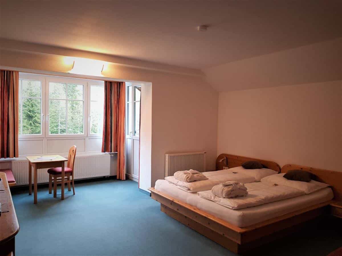 Twin beds with robes in a hotel room featuring a large window overlooking green trees.