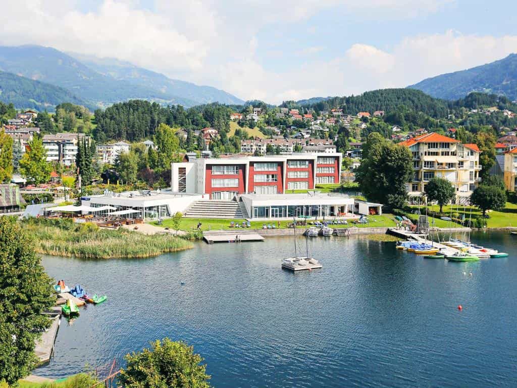 Hotel Royal on lake shore with sailboats, surrounded by green mountains and town buildings.