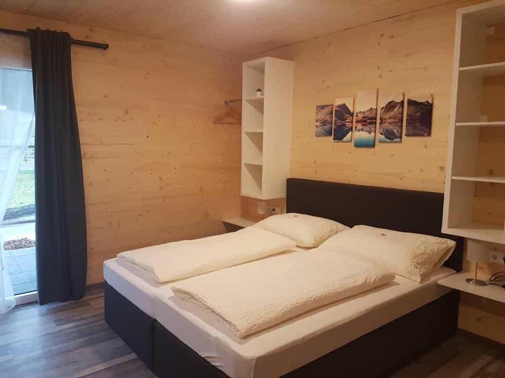 Double bed with white linens in a room with light wood paneling at Gästehaus am Hahnenkamm.