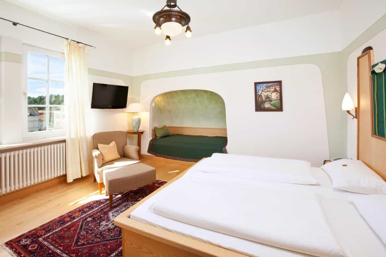 Hotel room with twin beds, built-in alcove bed, armchair, and window view.