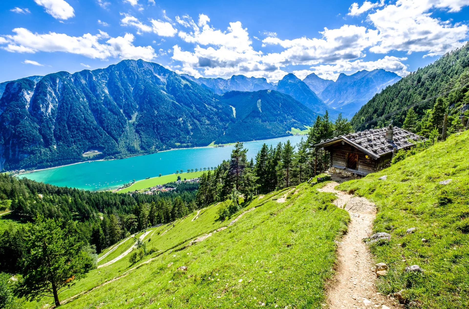 Hiking trail past wooden hut overlooking turquoise Achensee lake and blue mountains