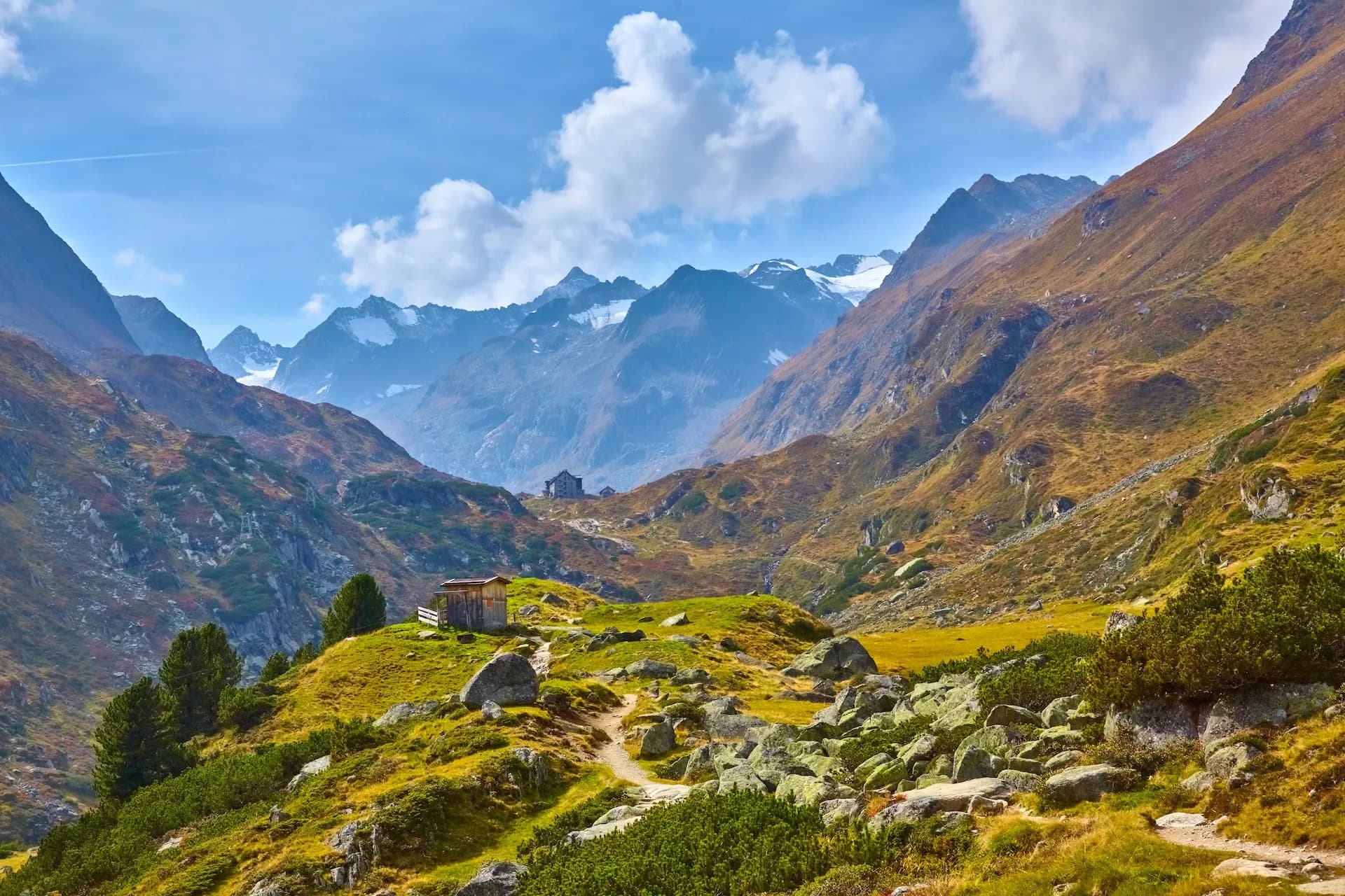 Alpine valley with rugged mountains, autumn colors, and small wooden huts in Stubai Valley.