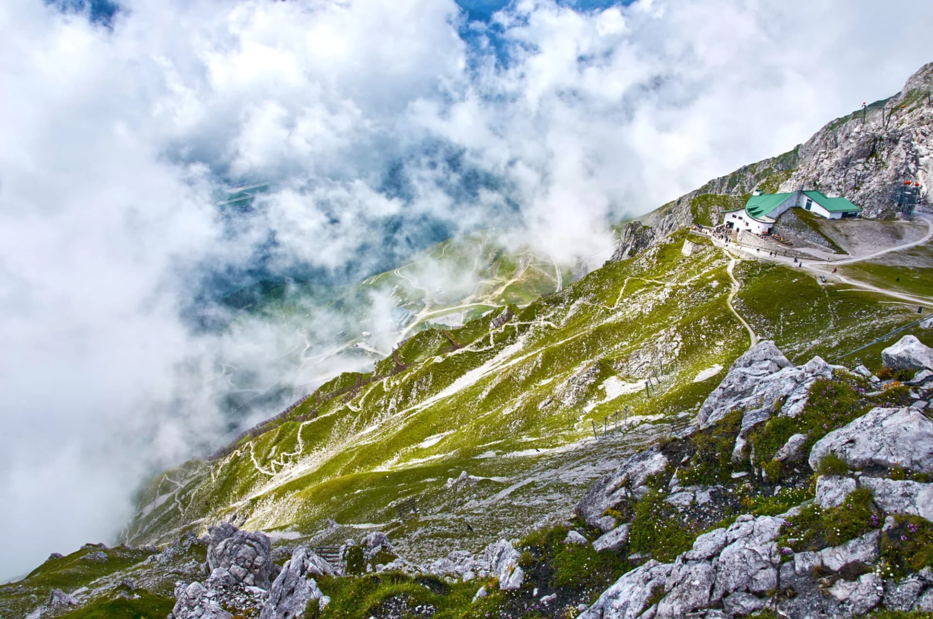 Hiking above Innsbruck with a mountain station building surrounded by clouds and green slopes.
