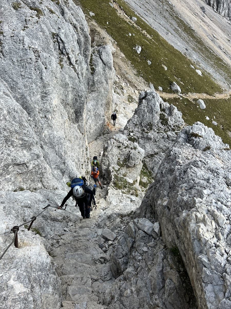 Hikers ascending steep rocky path with fixed cables on a mountain slope