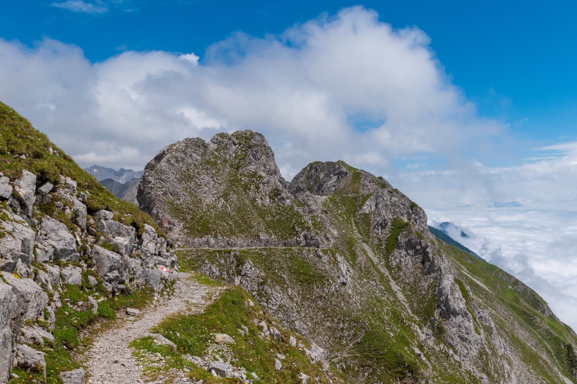 Hiking on Goetheweg trail past rocky peaks above clouds in the mountains