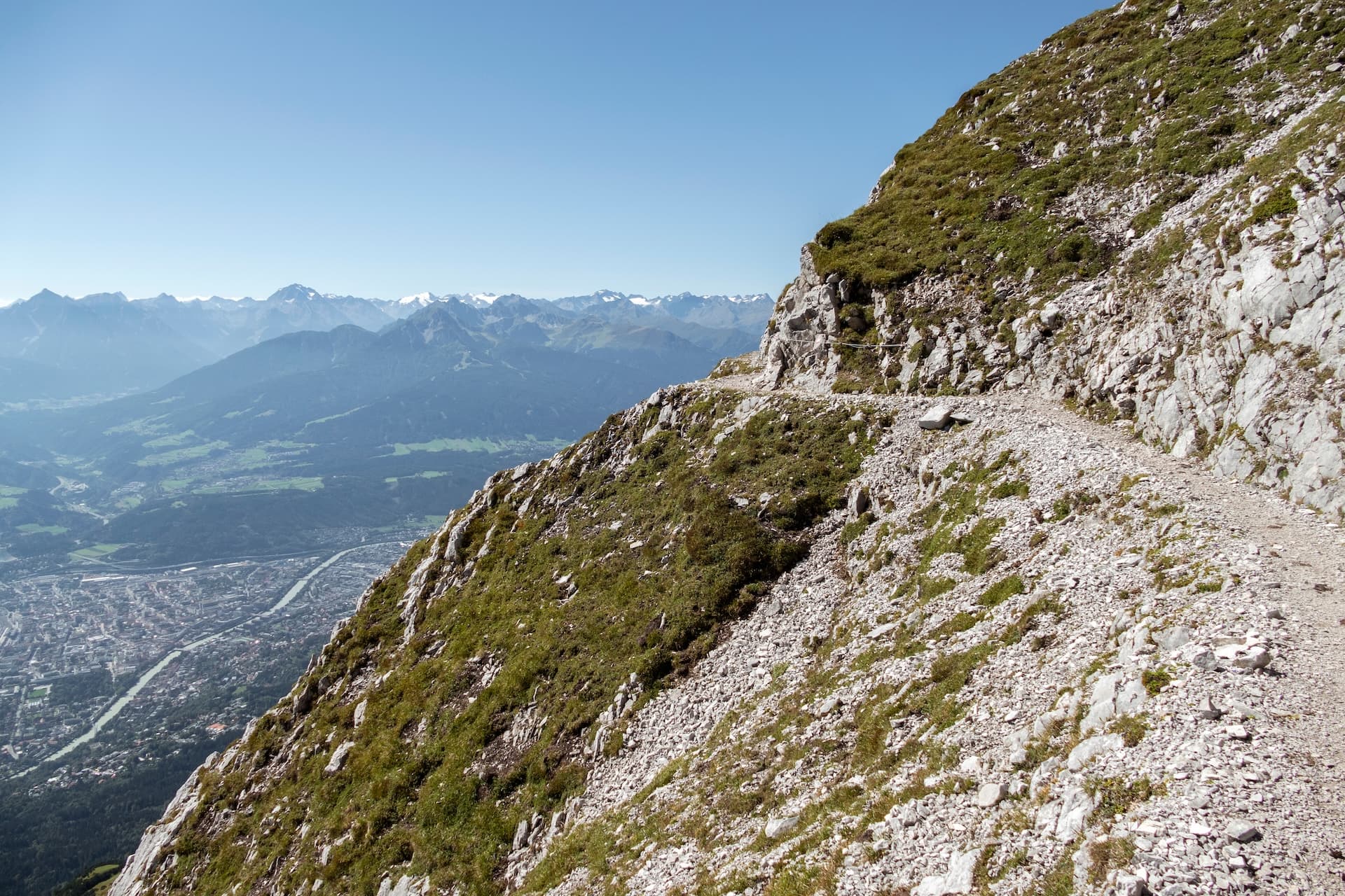 Hiking trail on exposed mountainside overlooking Innsbruck valley and snowy Alps.