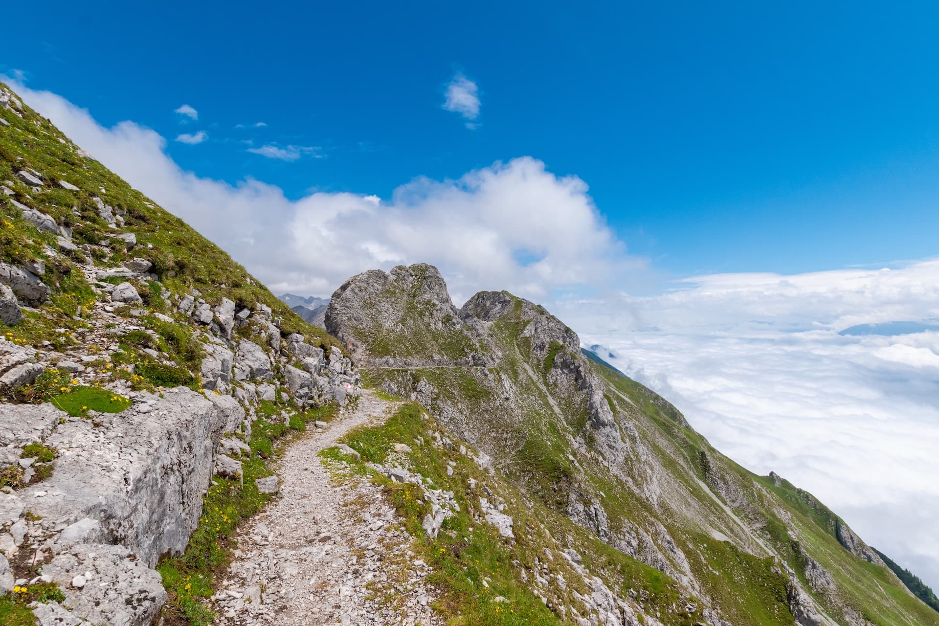 Hiking trail along steep, grassy mountainside above clouds on the Goetheweg in Innsbruck.