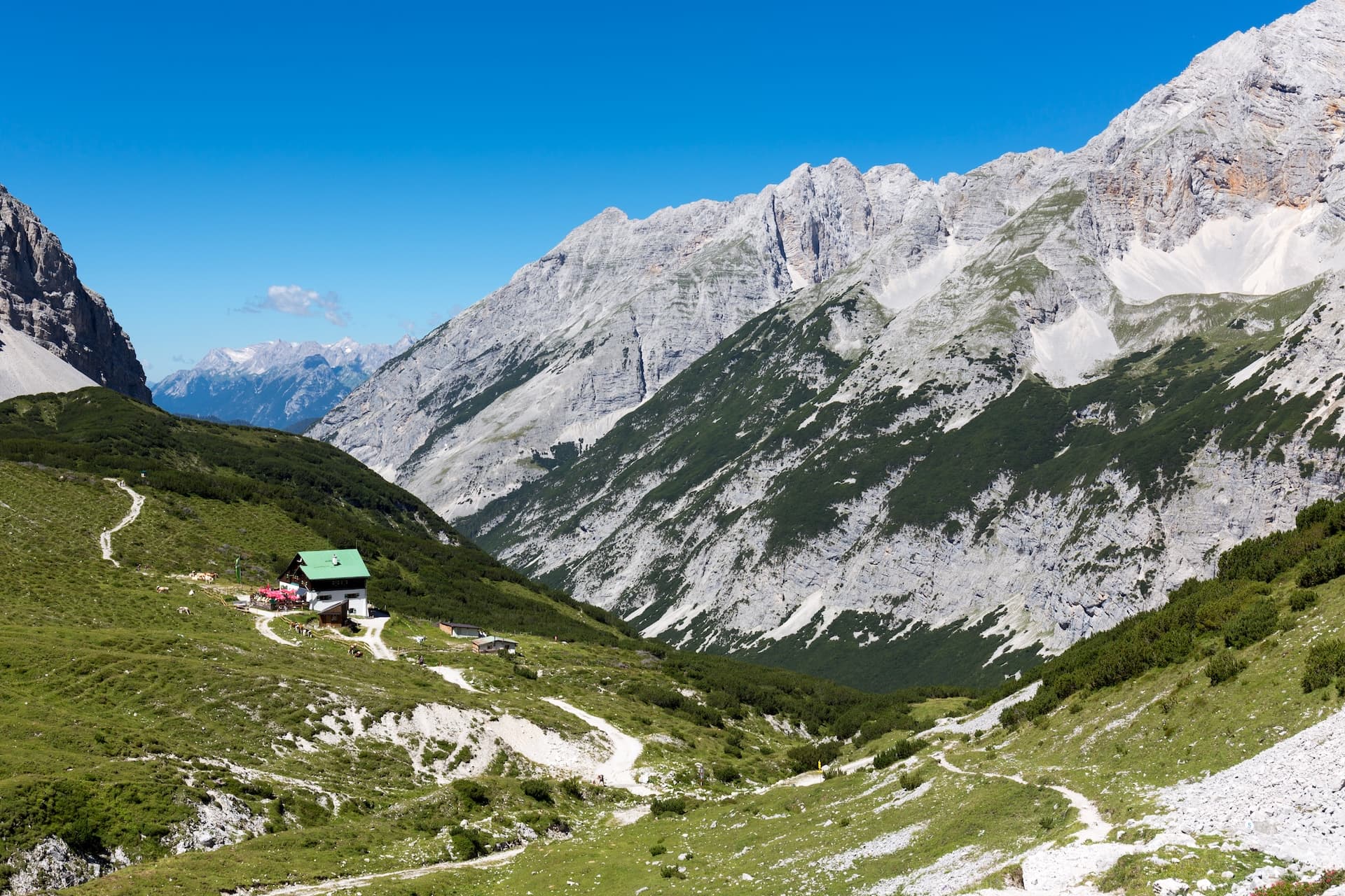 Alpine hut with green roof on grassy slope below massive grey mountains above Innsbruck