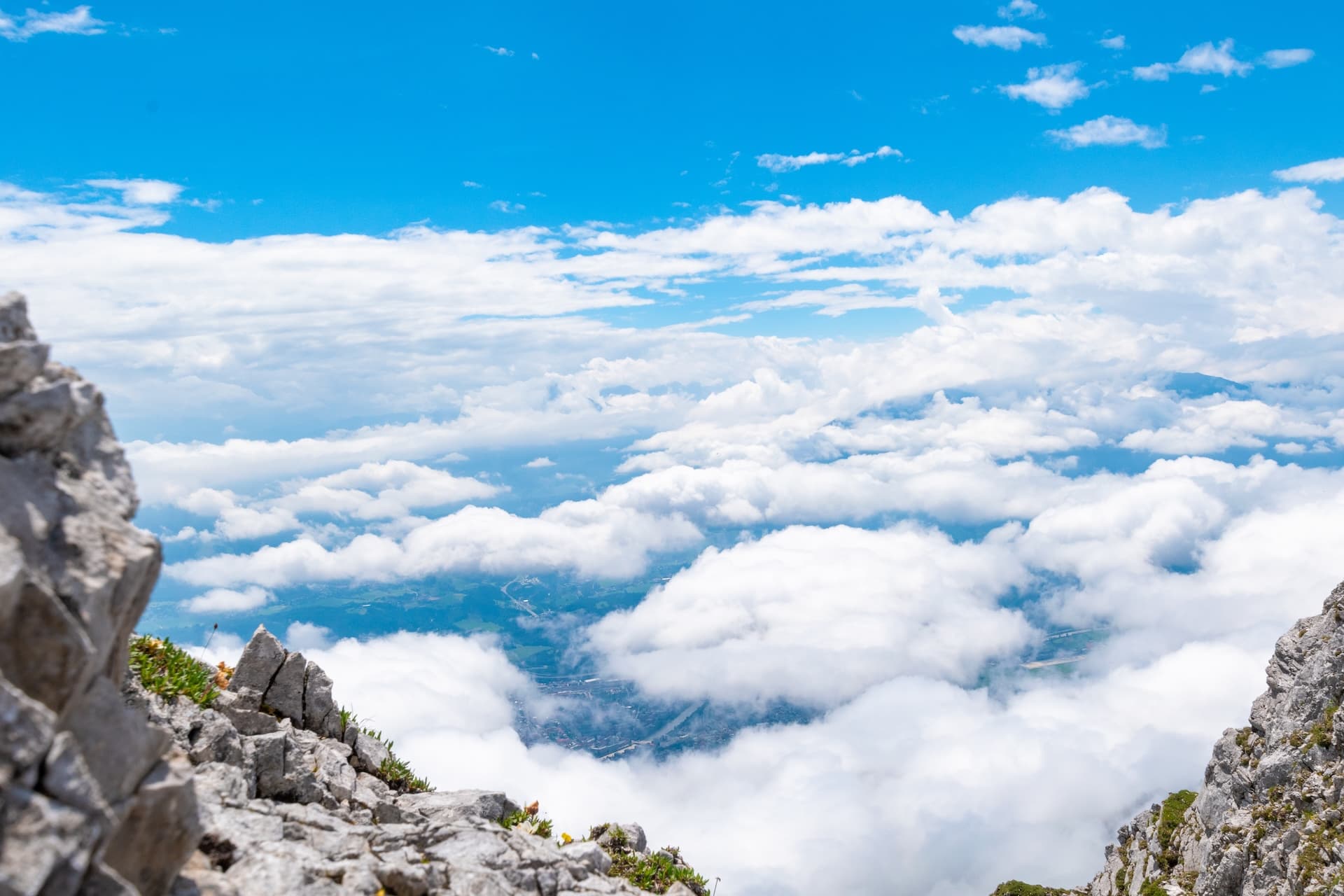 Rocky mountain peak view above clouds overlooking Innsbruck valley on a sunny day.
