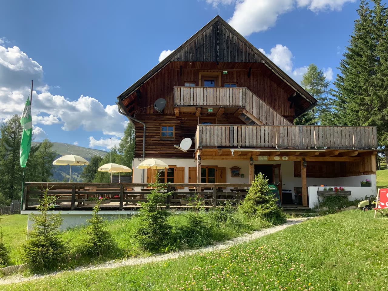 Neue Bonner Hütte alpine mountain hut with wooden balcony, terrace, and umbrellas in a grassy meadow.