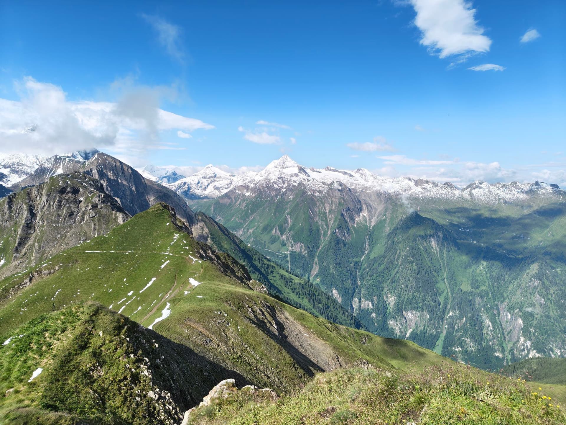 Green alpine ridge leading to snow-capped mountains under a blue sky at Brandlscharte on Grossglockner.