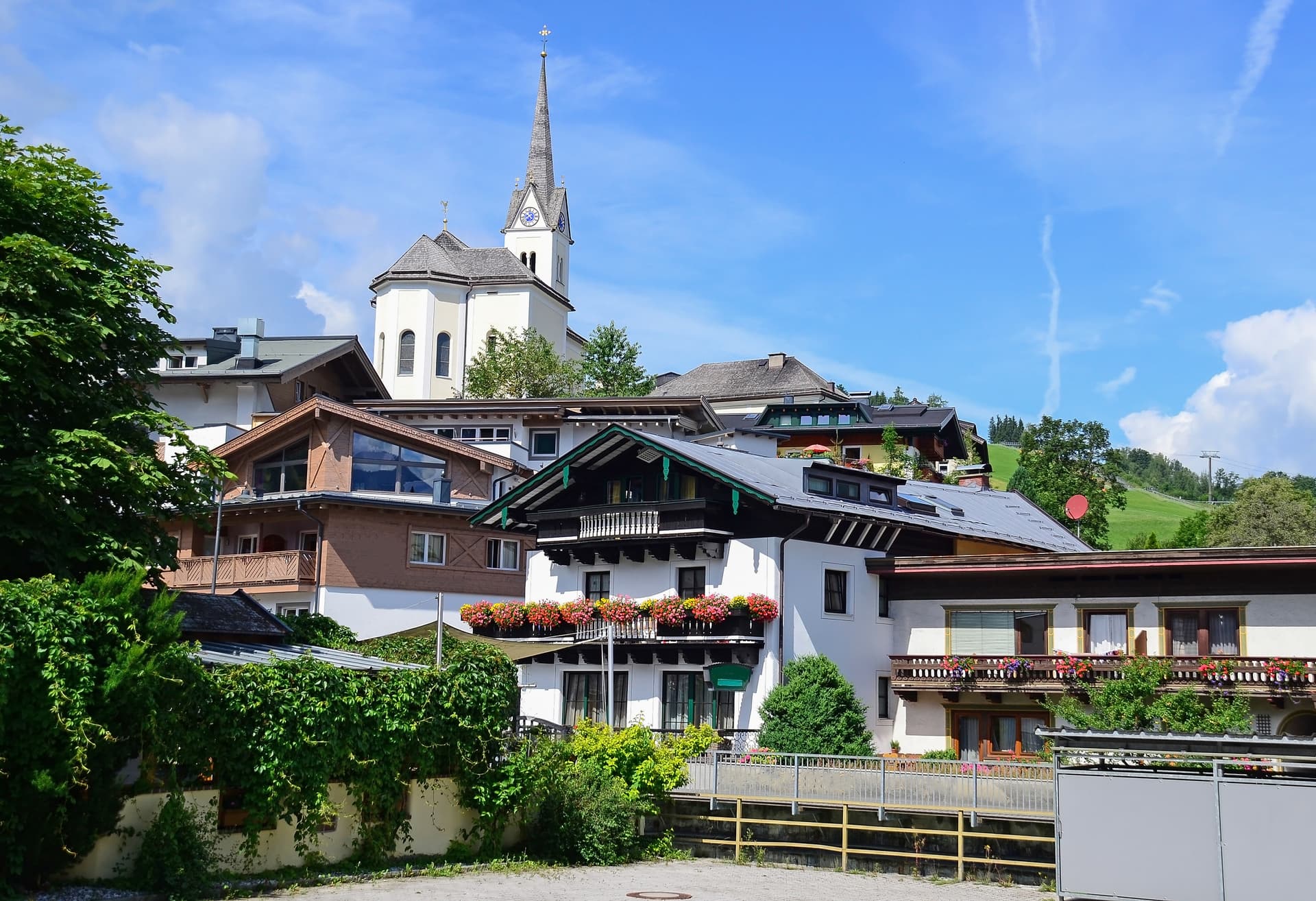 Alpine village buildings with a prominent church spire under a bright blue sky in Kaprun, Austria.
