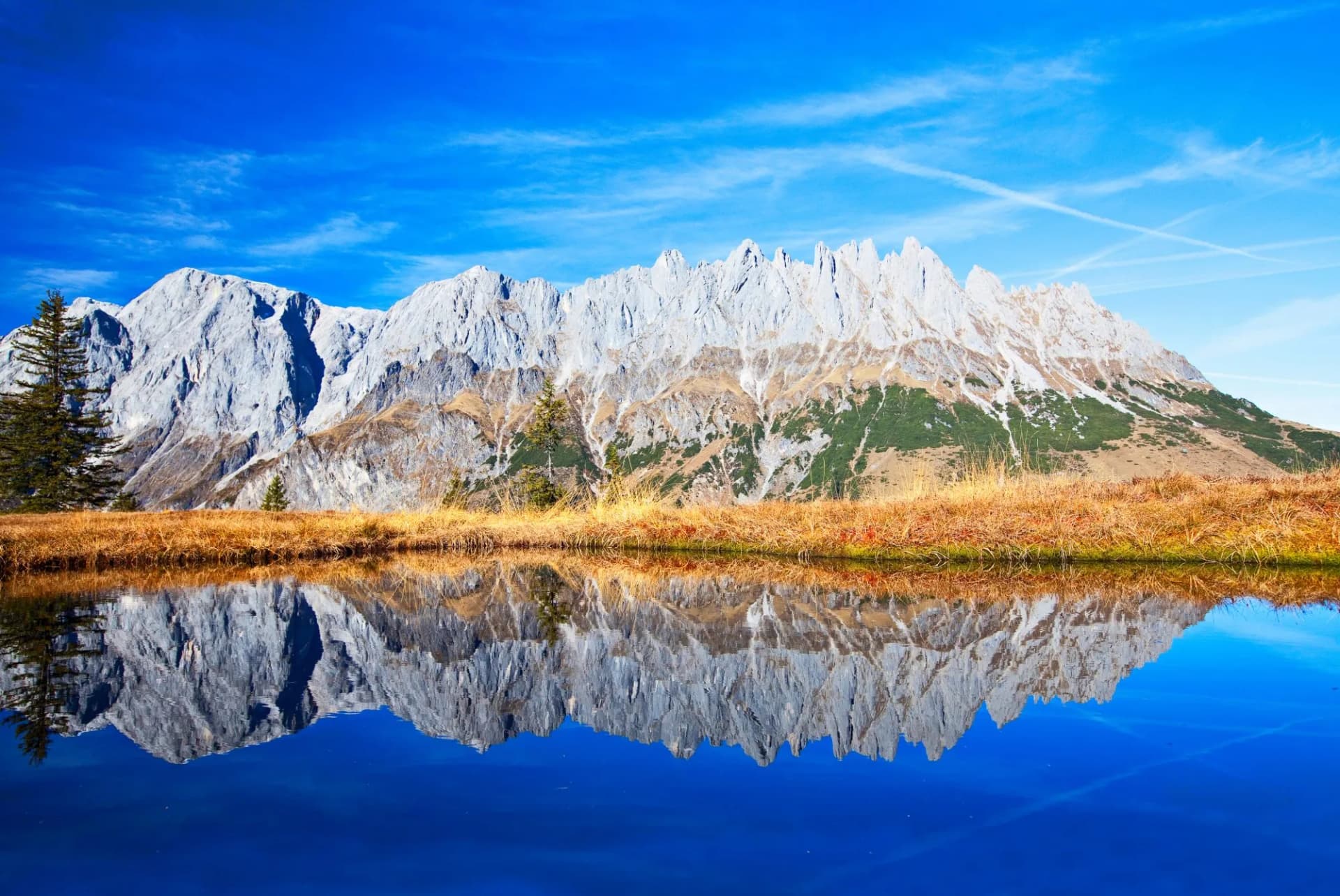 Hochkönig mountain reflection in a clear blue alpine lake with autumn grass.