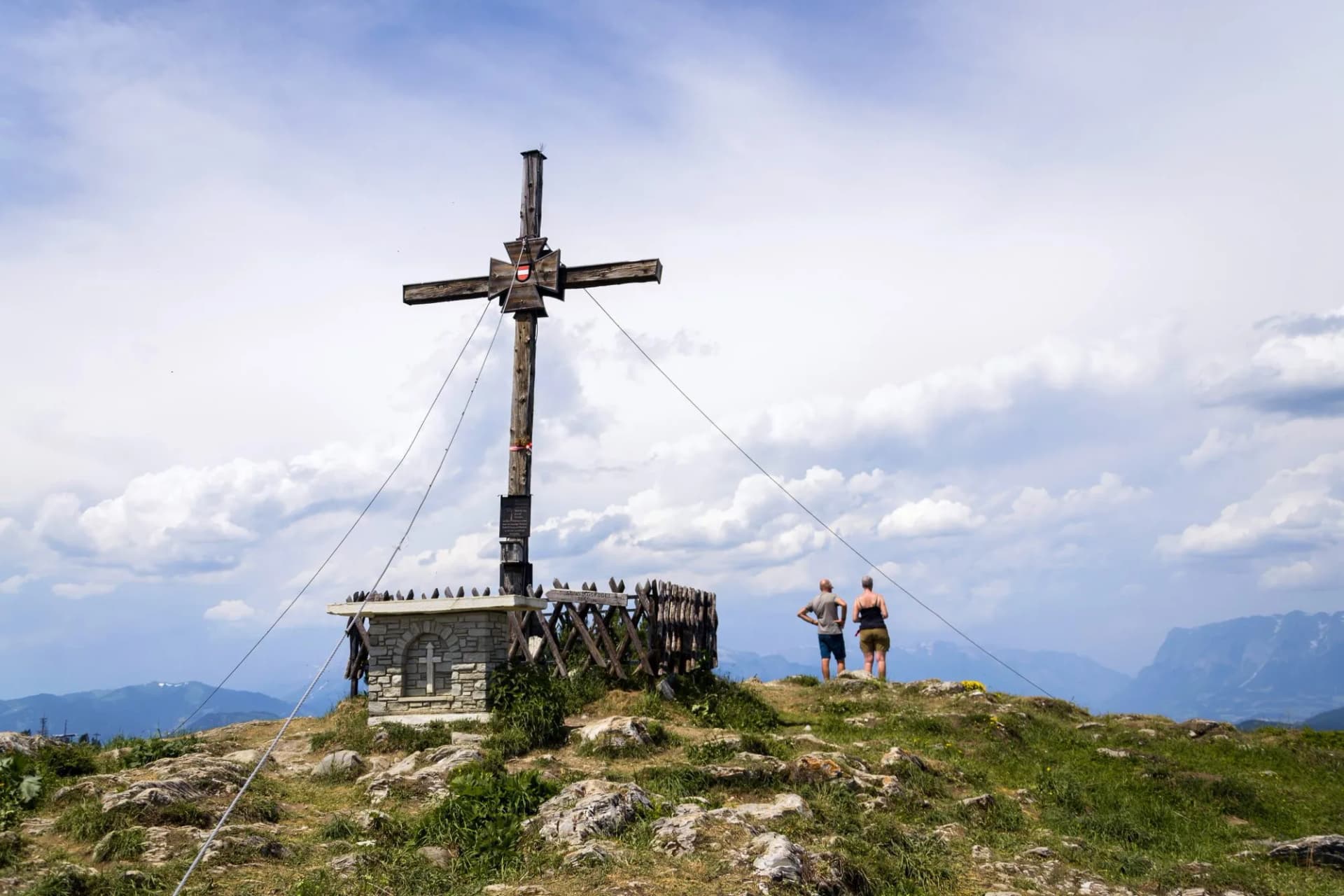Unrecognizable couple standing in front of the religious cross on Sonntagskogel Mountain summit in Alps, Sankt Johann im Pongau district, Salzburg federal state, Austria
