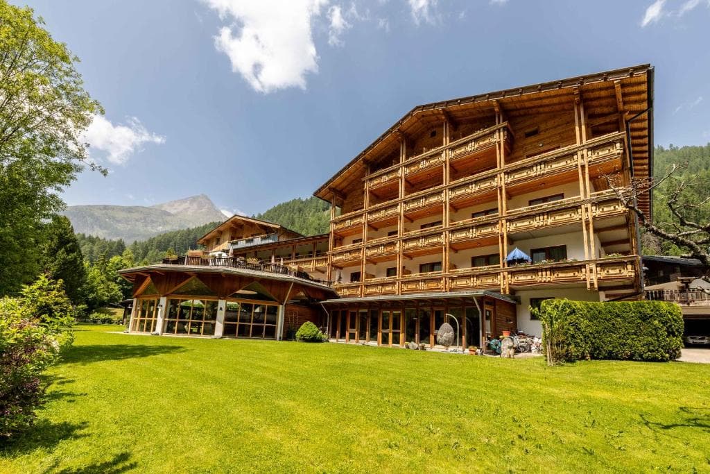 Hotel Kärntnerhof wooden building with balconies and large lawn in an alpine mountain setting.