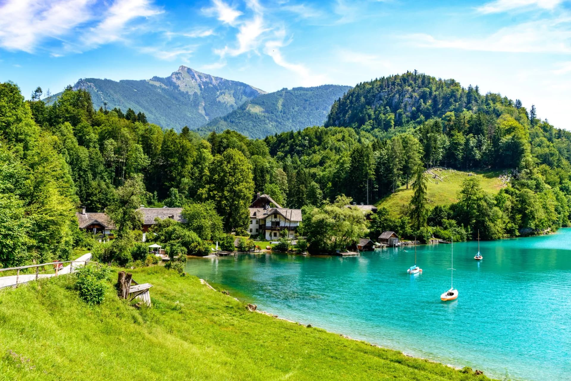 Sailboats on turquoise Wolfgangsee lake by St. Gilgen with green mountains and houses.