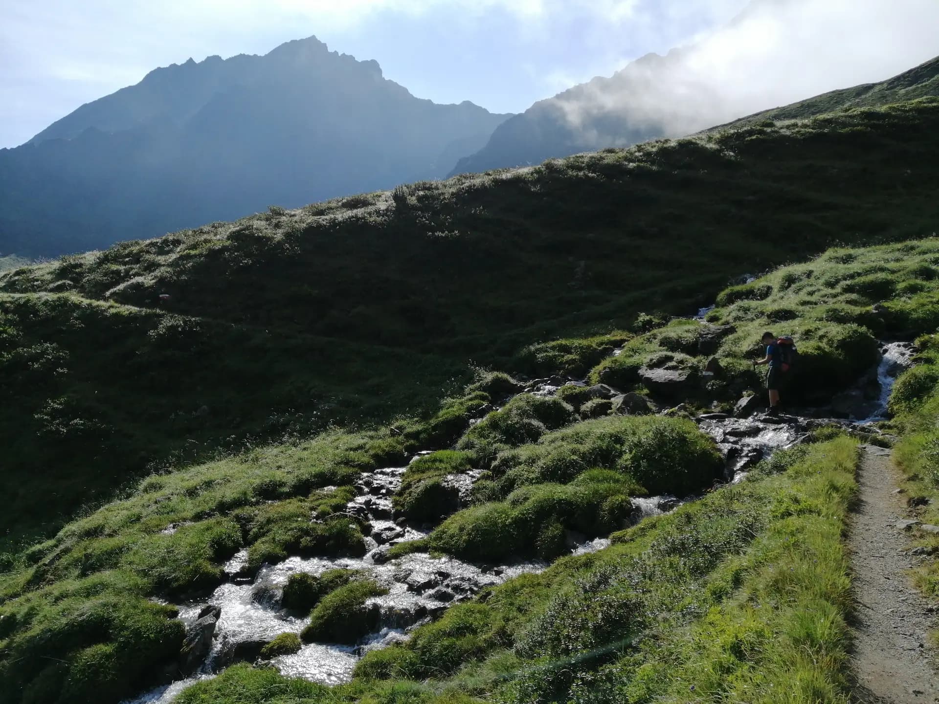 Hiker with a backpack crossing a small mountain stream on a trail in the Stubai Alps.