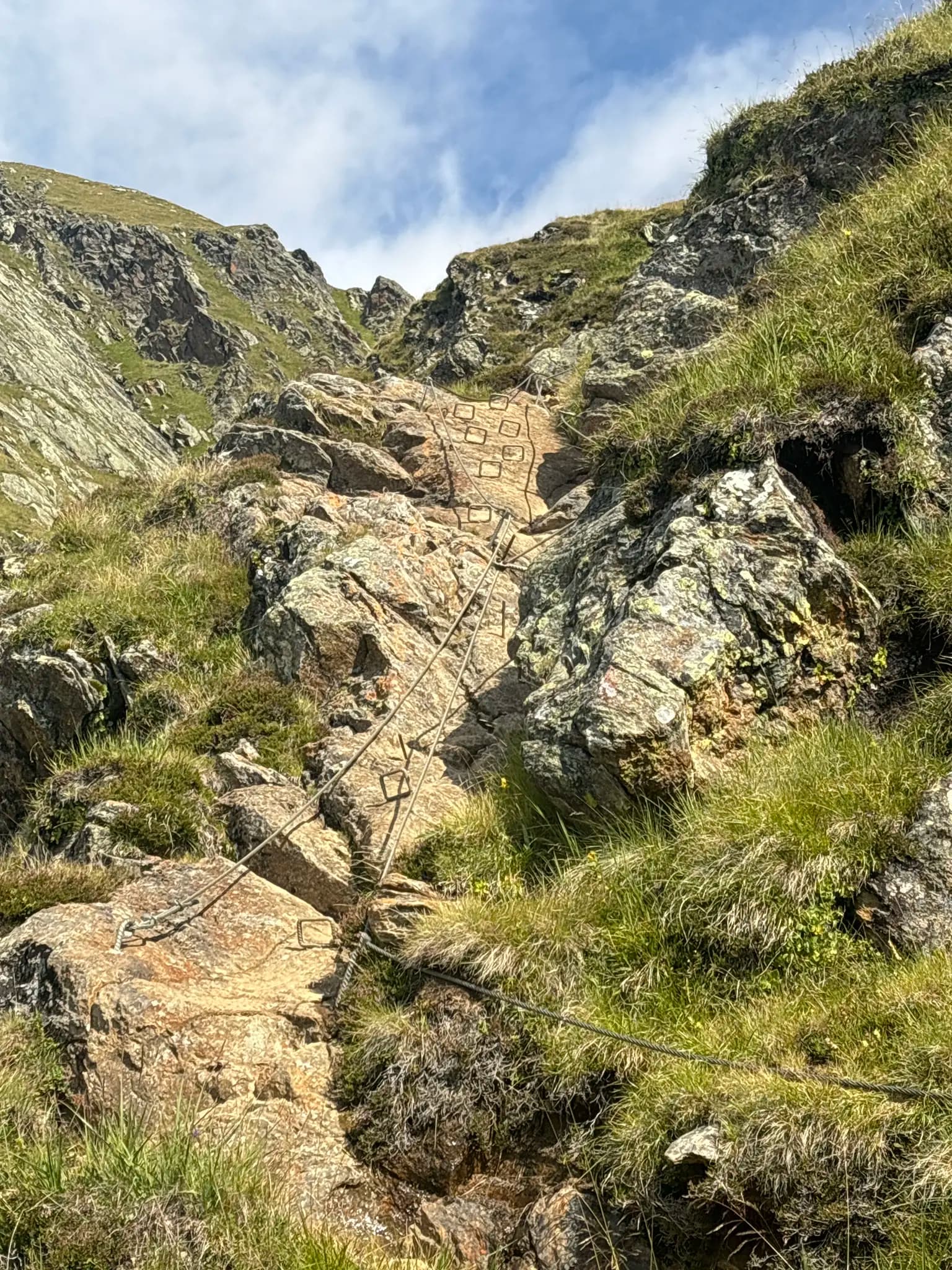 Via ferrata climbing route with metal rungs and safety cable on a steep, rocky alpine mountain slope.