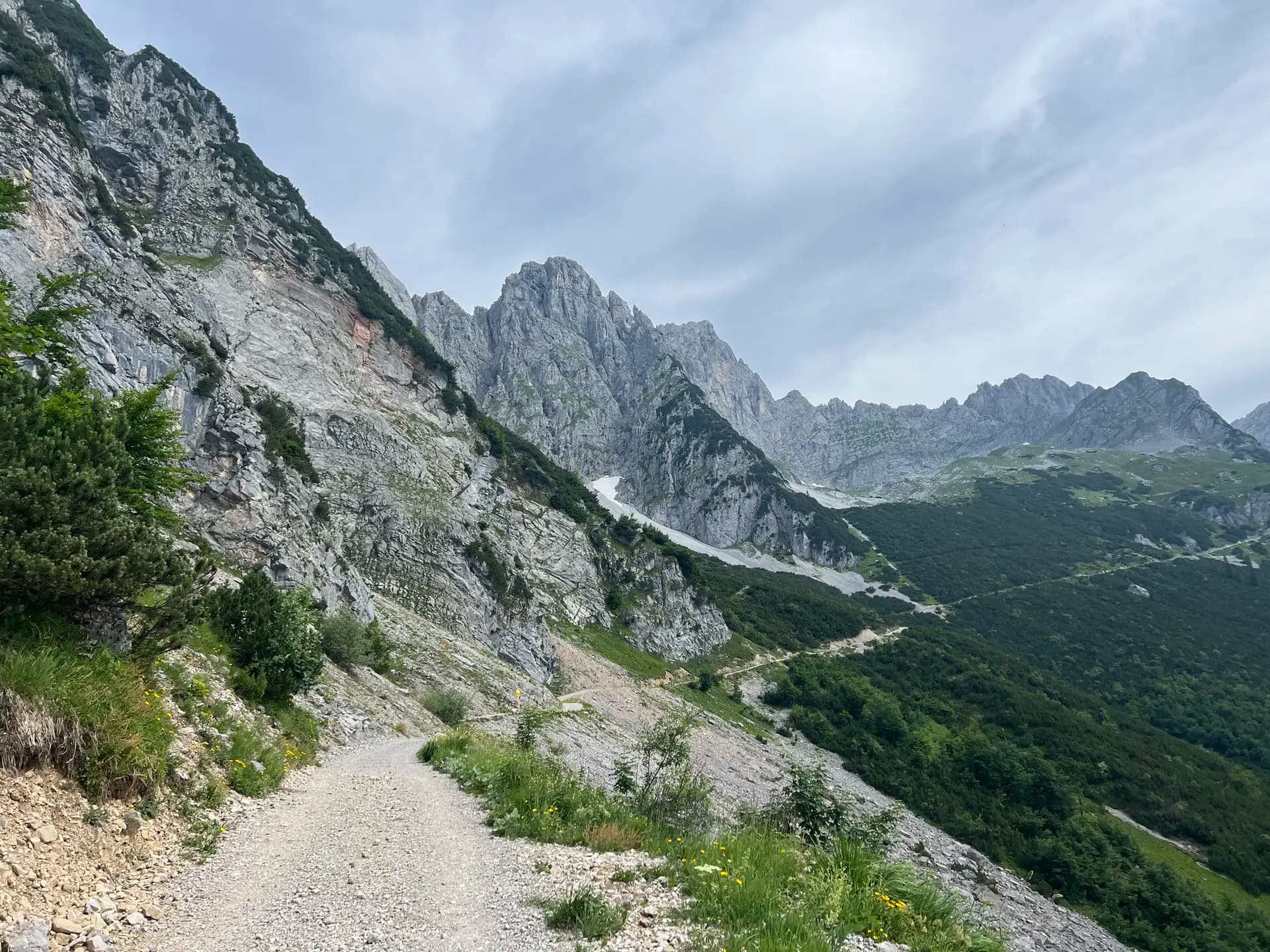 Gravel hiking trail winding through rocky Alpine mountain peaks with green forest slopes.