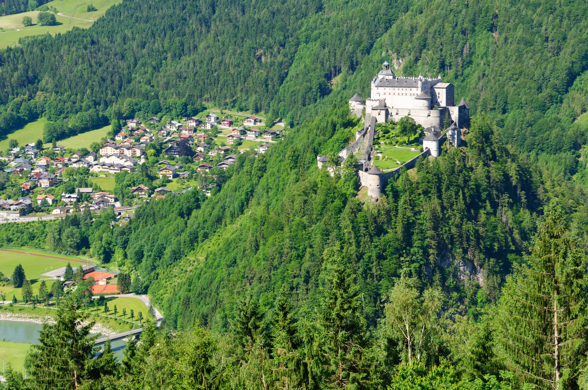 Hohenwerfen Castle perched on a forested hill above a small town in Austria.