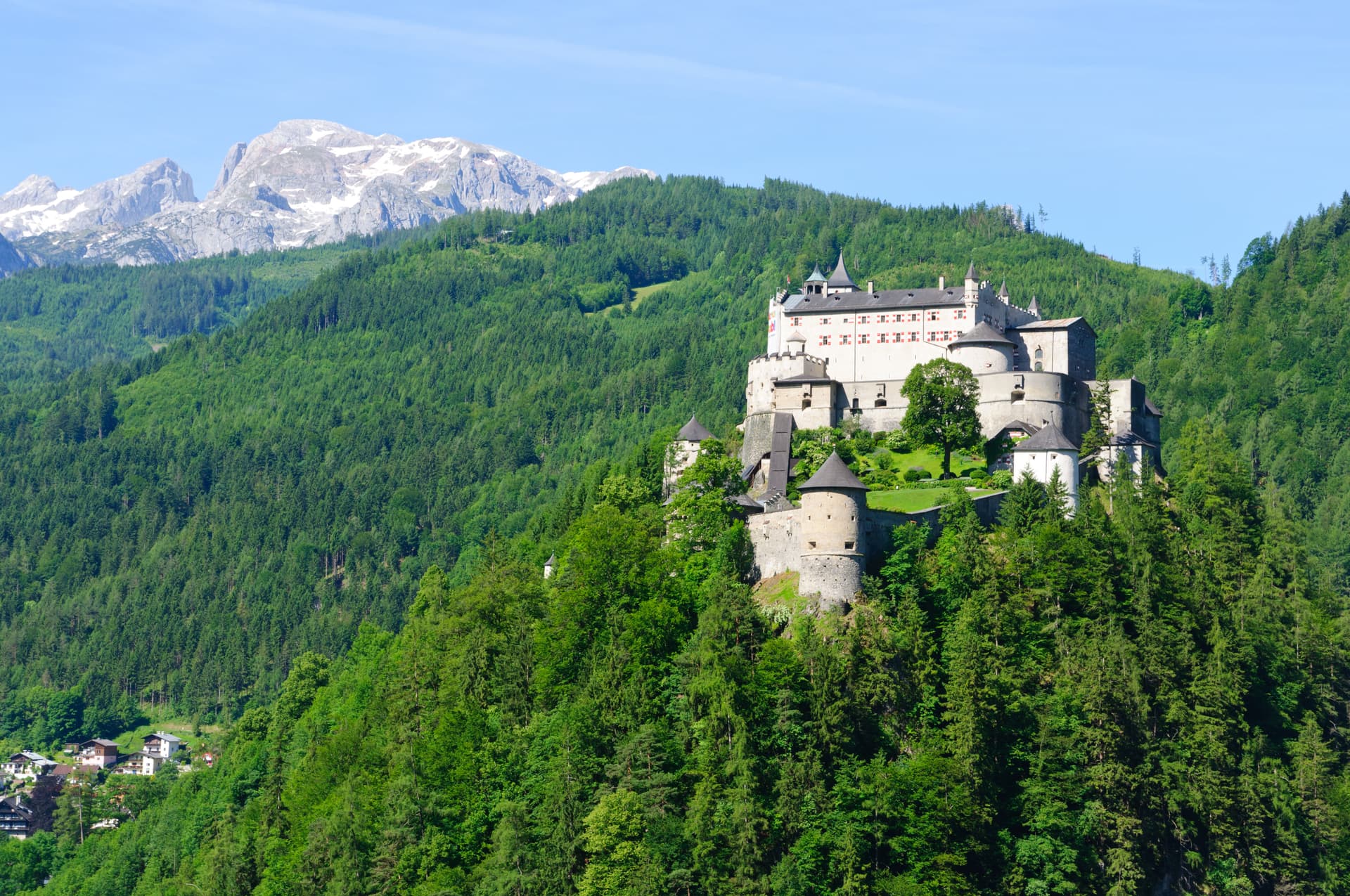 Hohenwerfen Castle perched on a green hillside below snow-capped mountains in Werfen, Austria.