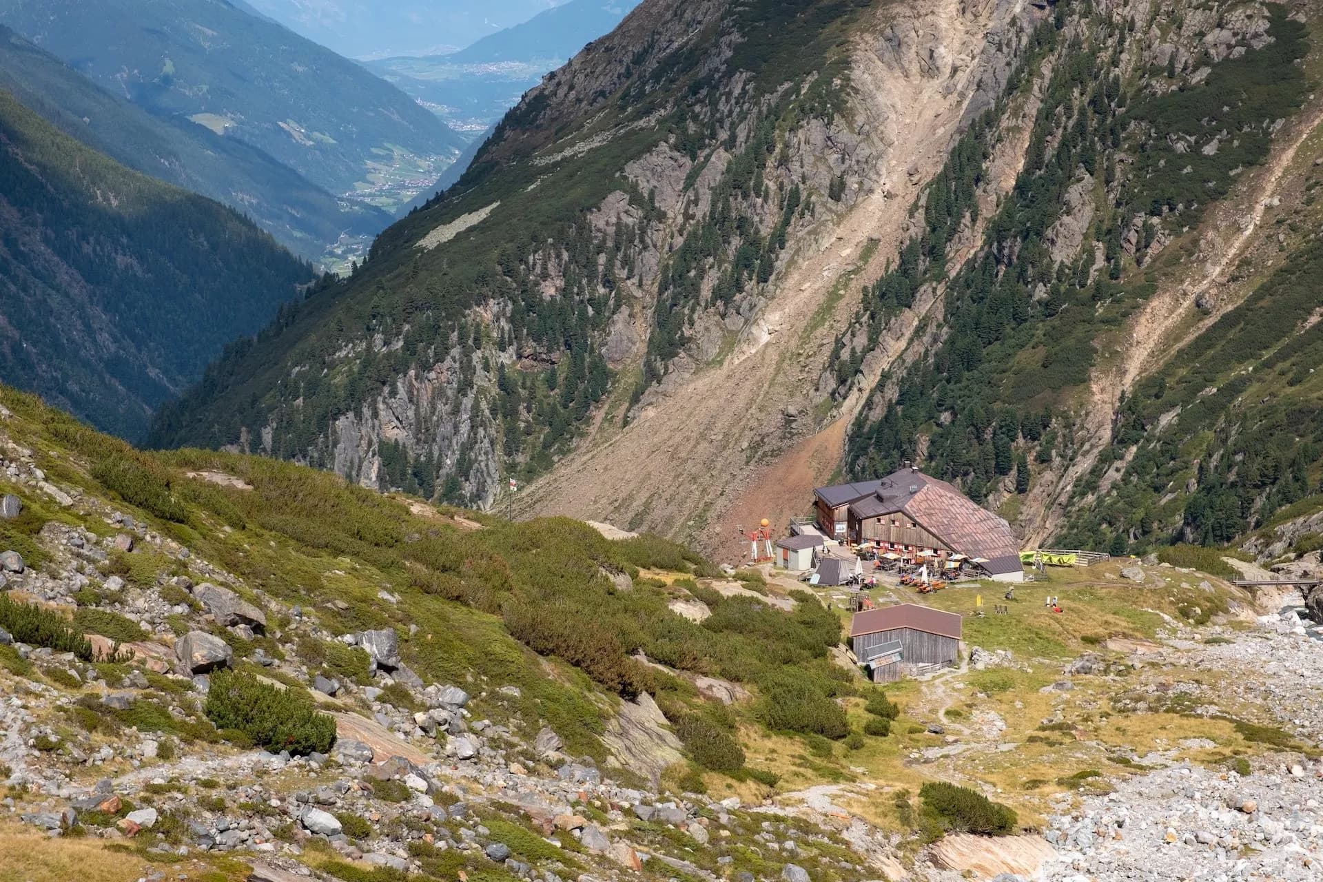 Alpine mountain hut nestled on a steep slope overlooking a deep valley with a village below.