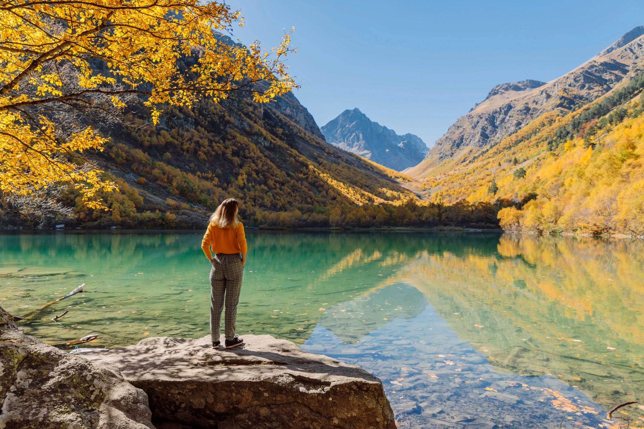Femme sur un rocher regardant un lac dans les montagnes automnales. Lac de montagne et fille voyageuse