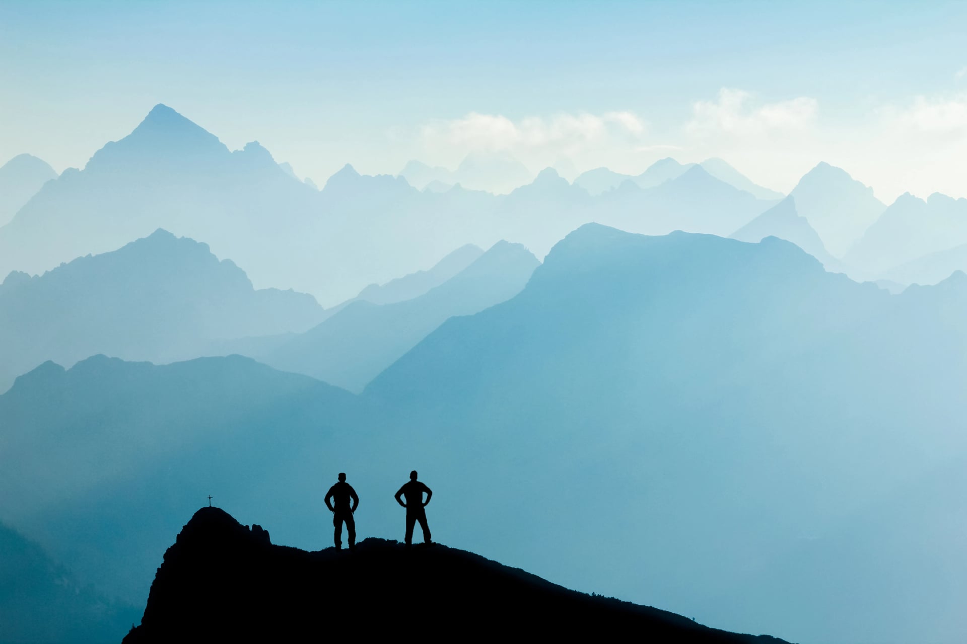 Deux hommes atteignant le sommet après avoir gravi et marché, profitant de la liberté et regardant vers les silhouettes des montagnes au lever du soleil.