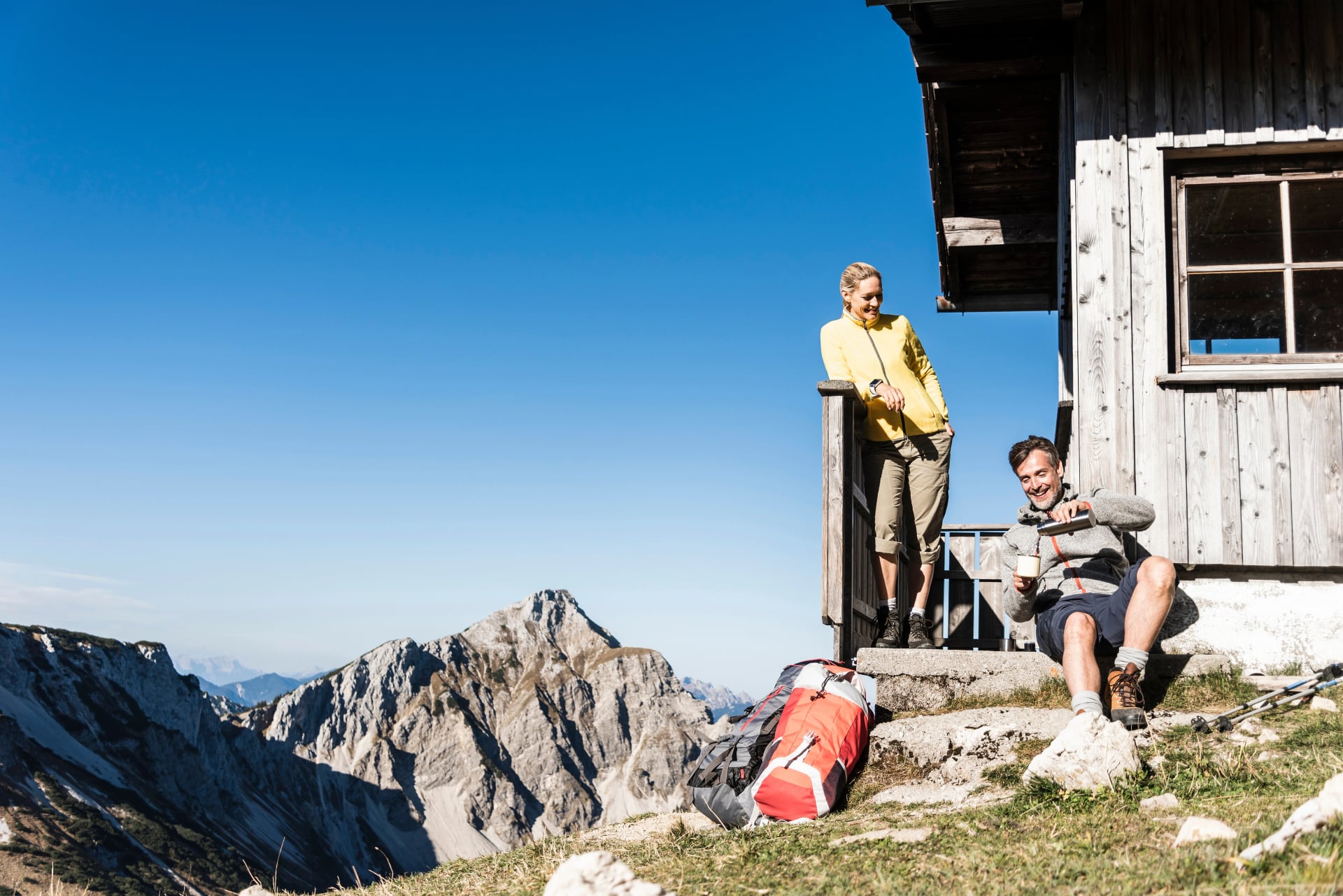 Couple de randonneurs assis devant un refuge de montagne, prenant une pause