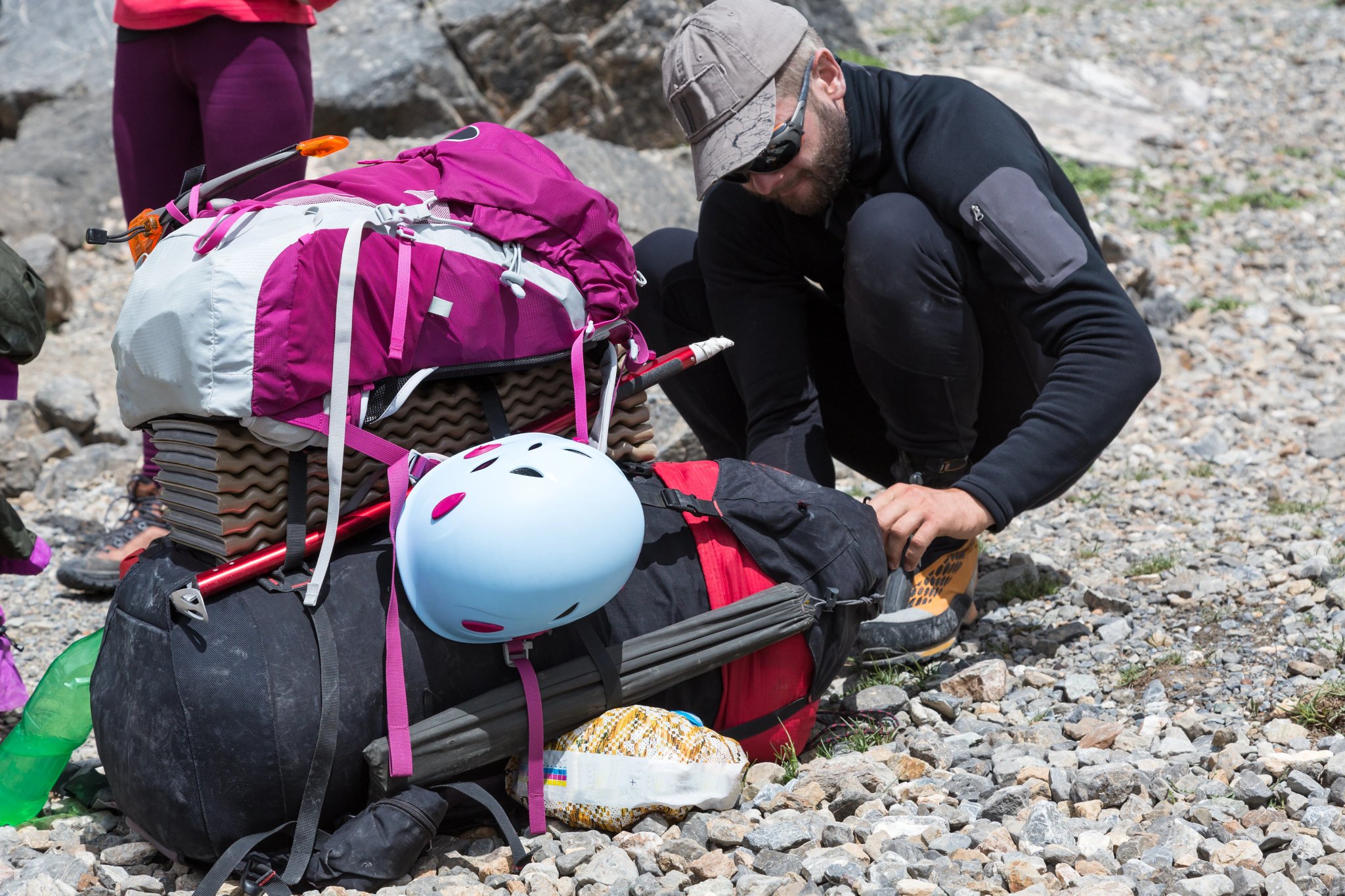 Randonneur préparant son sac à dos, homme barbu et grands et petits sacs à dos attachés l'un à l'autre avec casque d'escalade, piolet et autres équipements