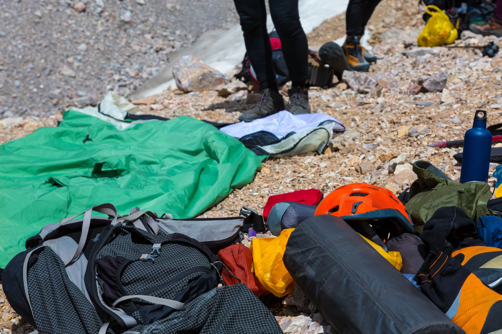 Équipement de randonnée en désordre, équipement d'escalade en montagne et de camping, sac à dos, casque, sac de couchage, bottes, thermos et autres jambes de personnes floues derrière