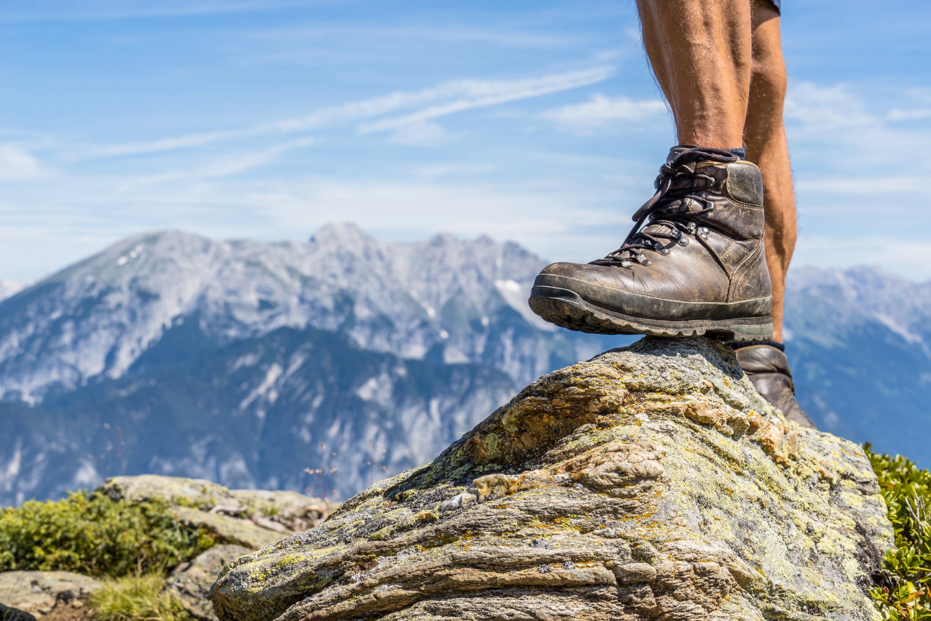Scarpa da escursionismo in pelle di un uomo che calpesta una piccola roccia nella valle dello Ziller, Austria. Raggiungendo la vetta con una bella catena montuosa alpina sullo sfondo
