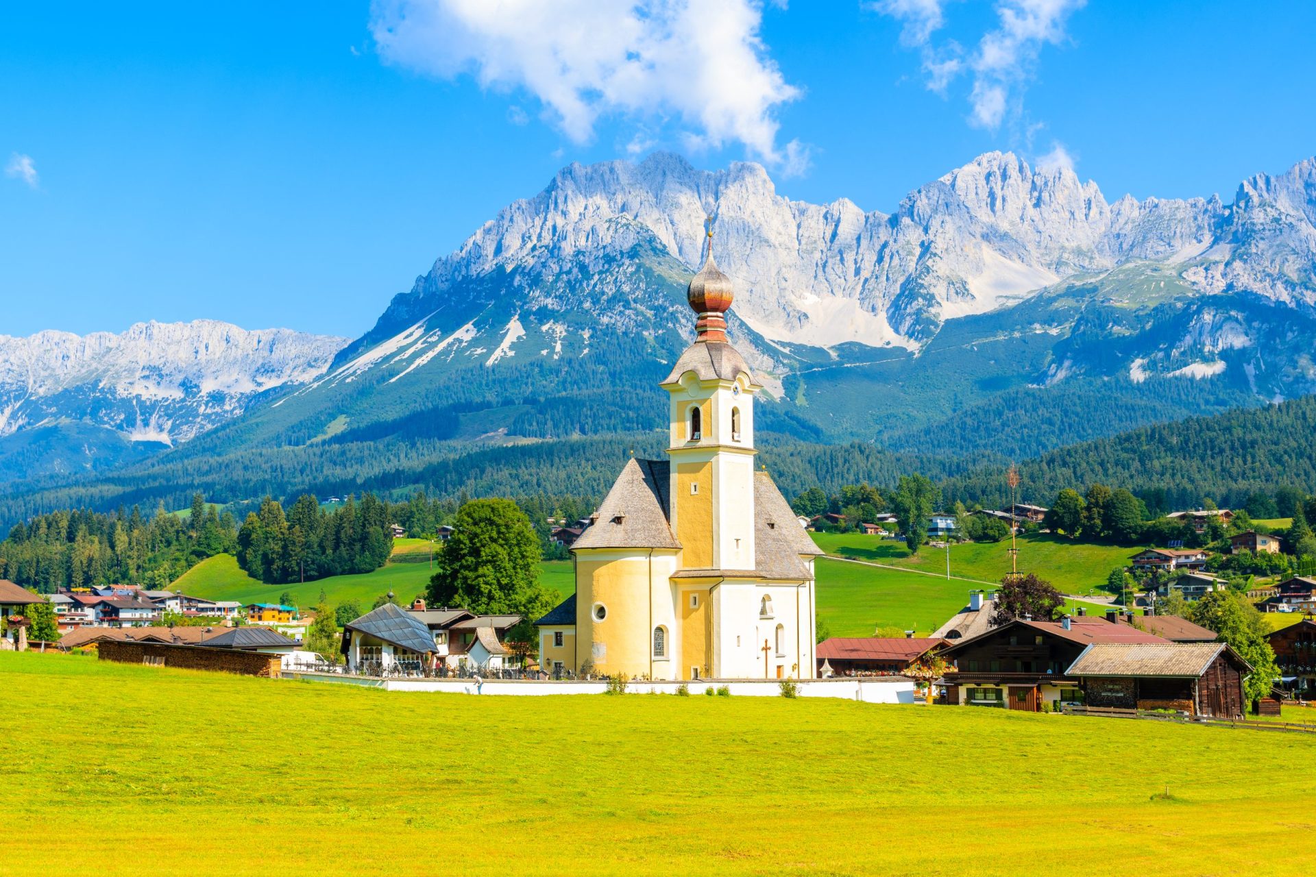Kirkko vihreällä niityllä Going am Wilden Kaiserin kylässä kauniina aurinkoisena kesäpäivänä, Tirol, Itävalta.
