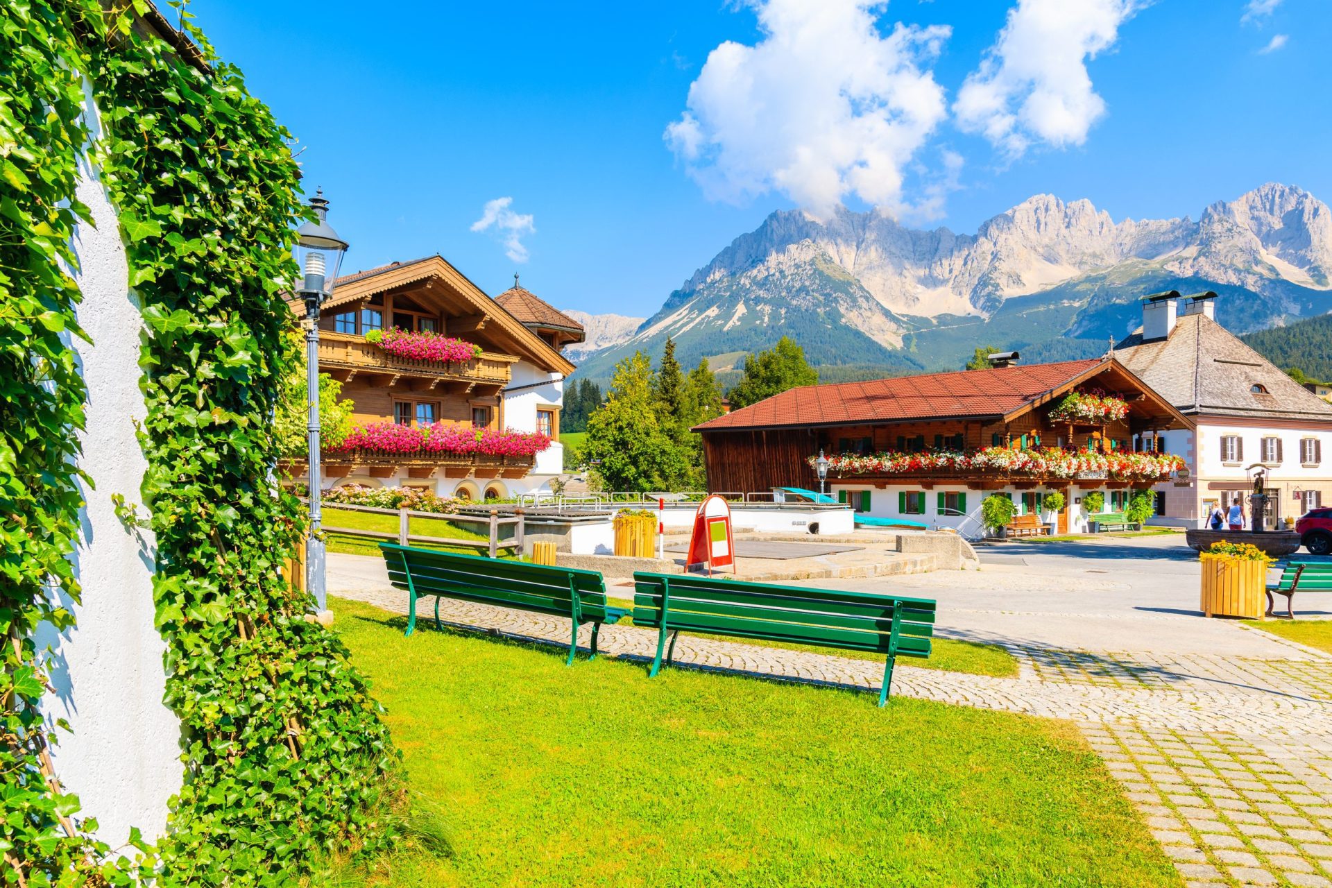 Traditionelle Alpenhäuser auf dem Dorfplatz von Going am Wilden Kaiser an einem schönen sonnigen Sommertag mit den Alpenbergen im Hintergrund, Tirol, Österreich